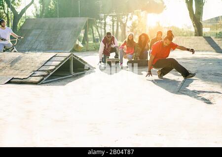 Group of happy friends listening music and watching breakdancer perfoming in city skate park - Young people having fun - Hip hop lifestyle concept - F Stock Photo