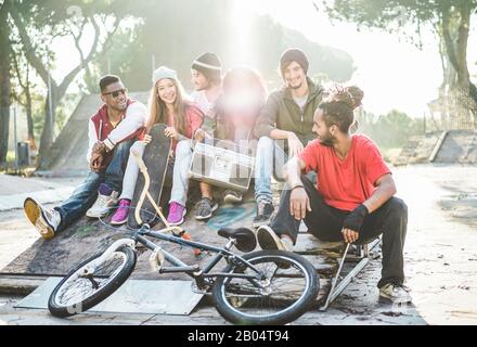 Young friends listening music and laughing in city park - Group of multiracial millennial people having fun together - Youth, urban lifestyle, multira Stock Photo