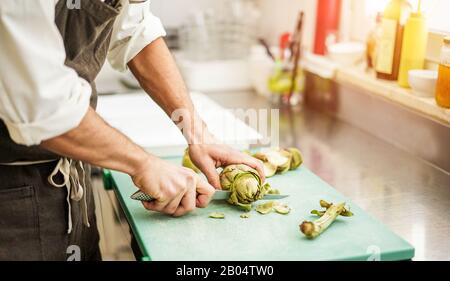 Chef cutting artichokes for dinner preparation - Man cooking inside restaurant kitchen - Focus on vegetable - Vegan cuisine, lifestyle and healthy foo Stock Photo