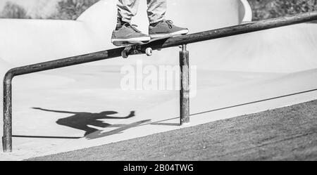 Skater performing tricks on ramp - Young man having fun doing extreme sport in skateboard park - Focus on feet - Black and white editing Stock Photo