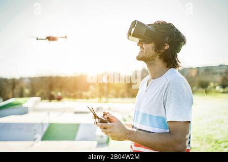 Bearded man using a drone with remote controller wearing virtual reality glasses making photos and videos - Young guy having fun with new vr technolog Stock Photo