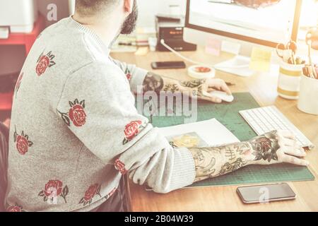 Tattoo artist creating new illustration with computer inside ink studio - Hipster tattoer working on flower draw - New fashion trends concept - Warm c Stock Photo