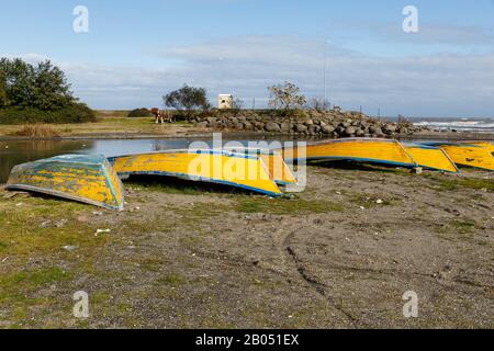 yellow fishing boats lie upside down on the sandy bank of the river, coast of the Caspian Sea Iran. Stock Photo