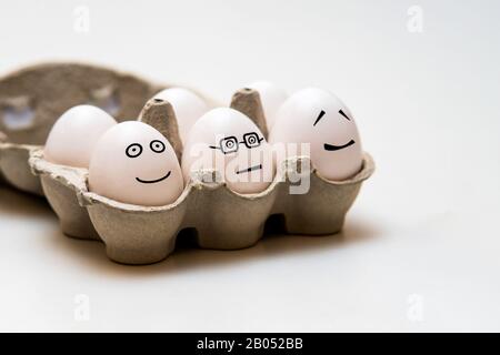 White eggs with funny faces in the brown small storage box on a light background Stock Photo