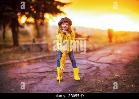 Happy funny child girl with umbrella in rubber boots at autumn park at sunset Stock Photo