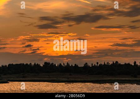 Sunlit clouds over the forest and river after sunset Stock Photo