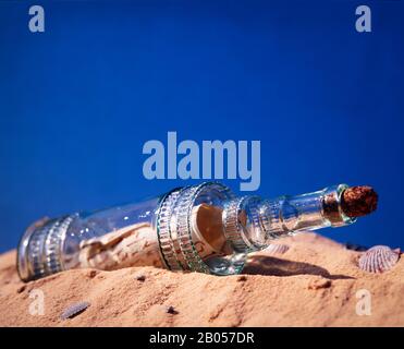 A message in a bottle lies on a white sand beach with blue sky in the background. Stock Photo