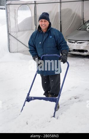 Man removing snow from his driveway with a sleigh shovel. Province of Quebec, Canada. Stock Photo