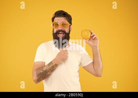 Man bearded hipster in orange sunglasses on yellow background. Cheerful guy hold ripe orange citrus fruit. Summer vacation. Refreshment source. Summer nutrition. Hipster with beard in summer mood. Stock Photo