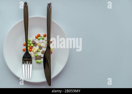 Pills on a white plate. Gesture with a knife and fork, bring the plaintive book, on a plate with pills. A pile of multi-colored tablets disguised as Stock Photo