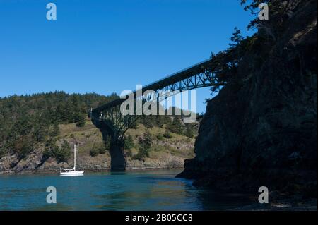 View of Deception Pass Bridge and sailboat from North Beach of Deception Pass State Park on Whidbey Island, Washington State, United States Stock Photo