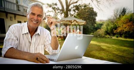 Portrait of mature man sitting at table with laptop. Stock Photo
