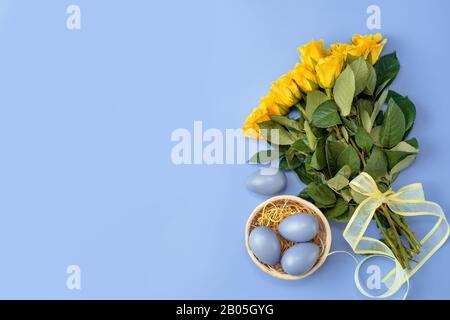 Yellow roses with blue Easter eggs on trendy colorful background Stock Photo