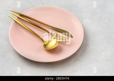 Beautiful pink plate and gold cutlery on grey background Stock Photo