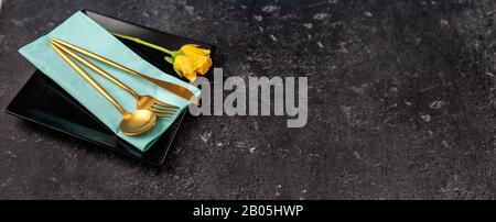 Set of stylish black square plate and gold cutlery on black background Stock Photo
