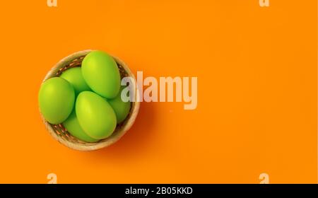 Easter concept. Simple composition with green eggs in basket on vibrant orange background Stock Photo