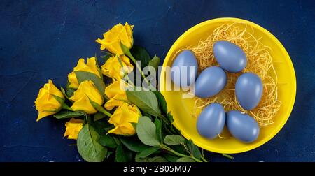 Close up of yellow roses and Easter eggs in a plate on trendy dark blue background Stock Photo
