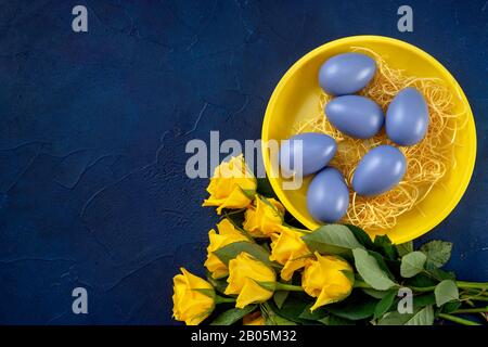 Easter composition with yellow roses and eggs on dark blue background Stock Photo