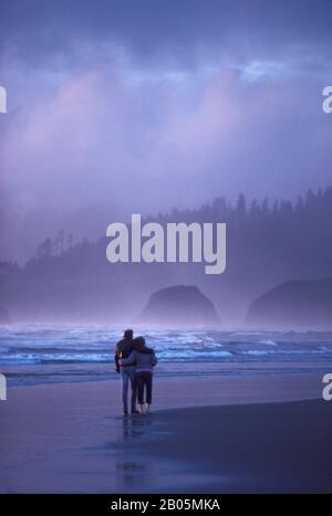 USA, OREGON, CANNON BEACH, COUPLE WALKING ALONG BEACH IN EVENING LIGHT Stock Photo