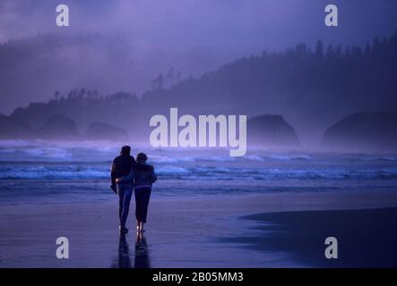 USA, OREGON, CANNON BEACH, COUPLE WALKING ALONG BEACH IN EVENING LIGHT Stock Photo