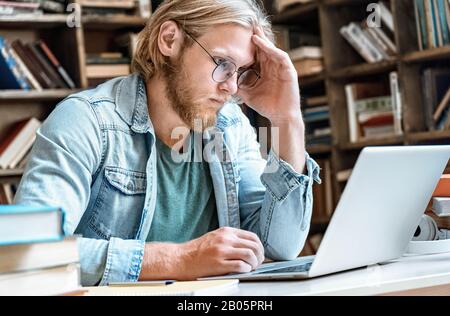 Young concentrated student home library desk read look at modern laptop Stock Photo