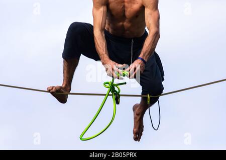 A low angle shot of a muscular man performing high wire stunts at a festival celebrating traditional cultures. Toned and bulging arms tie knots Stock Photo