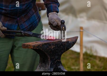 Closeup view on the hands of a traditional artisan at work. Metalworker uses blacksmith anvil and dated tools during an alternative community festival Stock Photo
