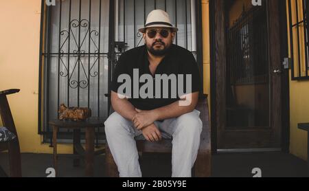 Chubby handsome Mexican man with fedora style hat, sitting wearing aviator glasses Stock Photo