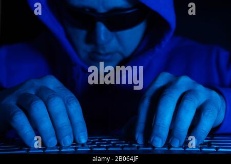 A man in glasses and a blue hoodie works at a computer. Soft focus Stock Photo
