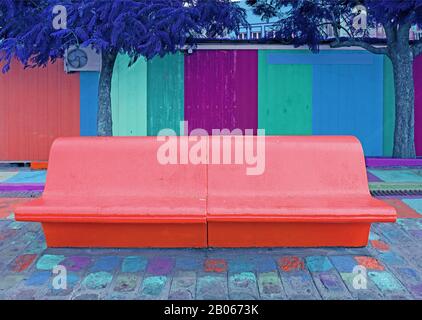 Pop art surreal styled concrete bench in coral pink with royal blue tree and colorful wooden wall in background Stock Photo