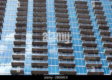Rows of balconies forming a repetitive pattern on the facade of the modern high rise building made out of the blue glass with sky reflection on it