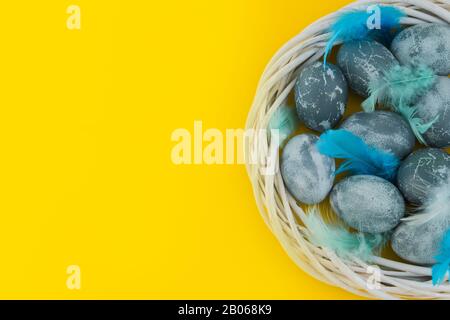 Blue textured colored Easter eggs with bird feathers in a nest or wreath on a bright yellow holiday background backdrop. Spring holiday concept. Copys Stock Photo