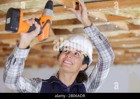 female builder using cordless drill overhead Stock Photo