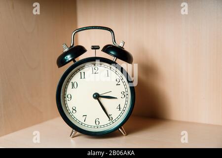 Black retro alarm clock stands on a light wooden shelf. Classic alarm clock. Stock Photo