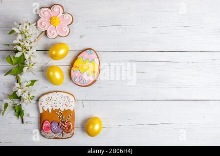 Festive Easter background or greeting card. Blooming Apple tree branch, painted yellow eggs, gingerbreads in form of Easter cake, flower and funny egg Stock Photo