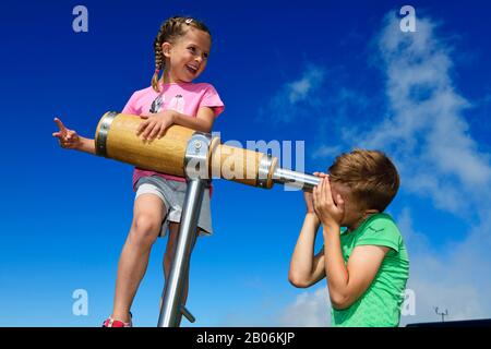 Girl and boy looking through a wooden telescope, summit panorama path of the Hohe Salve, Hopfgarten, Brixental, Kitzbuehel Alps, Tyrol, Austria Stock Photo