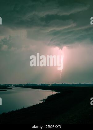 Angry sky over a river with lightning bolt striking down to earth Stock Photo