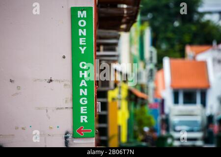 Money changer vertical green signboard with red arrow direction is mounted on the wall for tourists direction to change currency Stock Photo