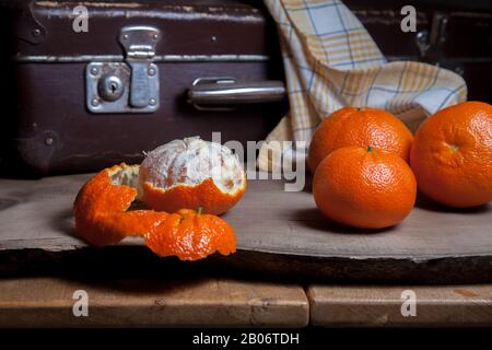 Several of whole fresh orange mandarine or oranges, tangerines, clementines, citrus fruits and one fruit is half peeled on wooden board Stock Photo