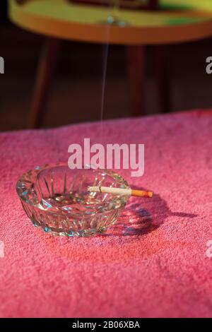 Ashtray with burning cigarette on sunbed with yellow table with cocktail and radio next to it. Stock Photo