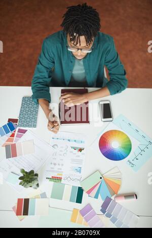 High angle view of African young designer sitting at his workplace and working with colored pattern Stock Photo