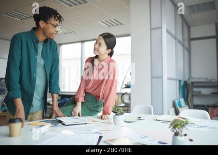 Two young designers looking at each other while working with sketches at the table in workshop Stock Photo