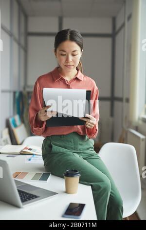 Serious young businesswoman sitting on her workplace and reading a business contract at office Stock Photo