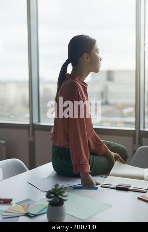 Young businesswoman sitting on the table looking at window and thinking over new ideas at office Stock Photo