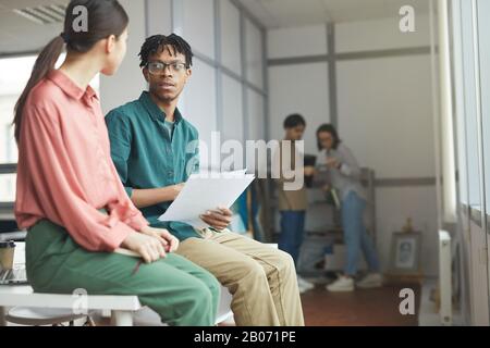 Two business colleagues sitting on the table and discussing report they preparing for the meeting together Stock Photo