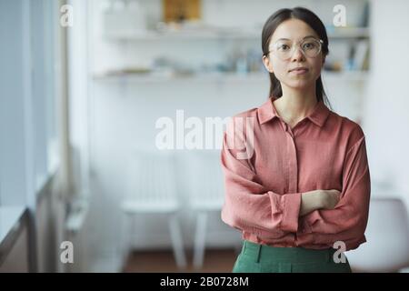 Portrait of confident young businesswoman in eyeglasses standing with arms crossed and looking at camera at office Stock Photo