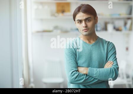 Portrait of young man in casual clothing standing with arms crossed and looking at camera at office Stock Photo