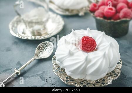 Delicious mini Pavlova meringue cake decorated with fresh raspberries, with a beautiful Cup lying on a platter. Stock Photo