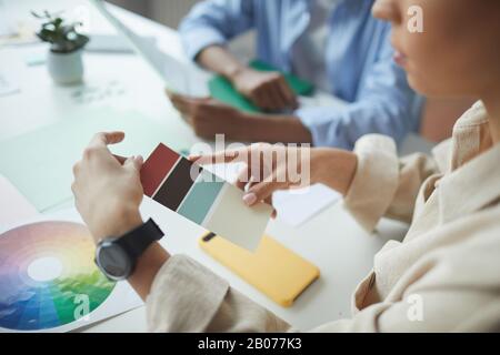 Close-up of businesswoman holding colored palette and choosing a color while sitting at the table with her colleagues Stock Photo