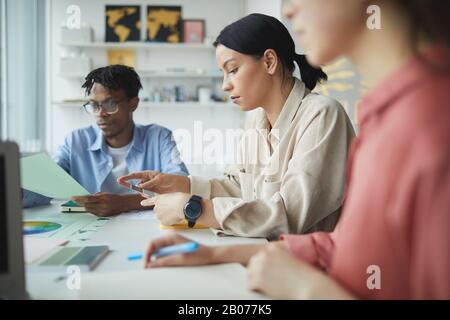 Serious young designer examining colored pattern together with her colleagues during a meeting Stock Photo